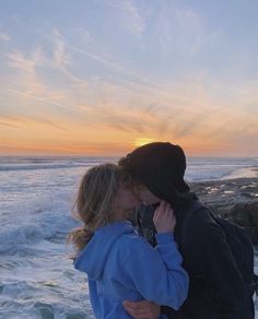 a man and woman are kissing on the beach at sunset with waves in the background