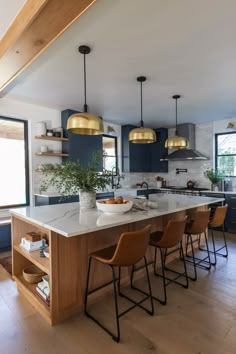 a kitchen with blue cabinets and gold pendant lights above the island countertop is surrounded by brown leather chairs