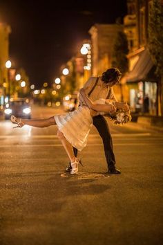 a man and woman are dancing on the street at night with their legs spread out