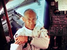 a pilot in the cockpit of an airplane with his hands on his chest and looking at the camera