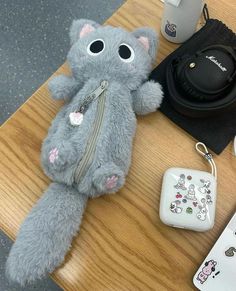 a gray teddy bear sitting on top of a wooden table next to a cup and headphones