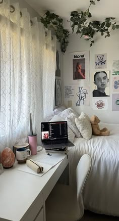 a laptop computer sitting on top of a white desk in front of a bed covered with pillows