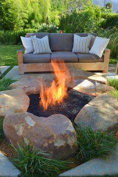 an outdoor fire pit surrounded by rocks and grass with pillows on it's sides