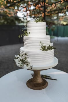 a wedding cake with white frosting and greenery on top is sitting on a table