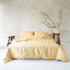 a bed with yellow sheets and pillows next to a plant in a vase on the floor