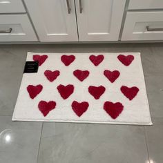 a white rug with red hearts on it in front of a kitchen cabinet and drawers