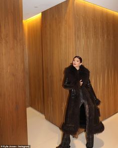 a woman standing in front of wooden walls wearing a black coat and fur stoler