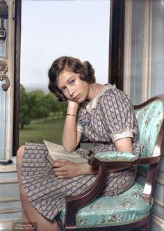 a woman sitting in a chair with her hand on her chin and reading a book