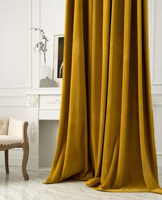 a chair sitting next to a window covered in yellow curtaines and drapes on a white wall