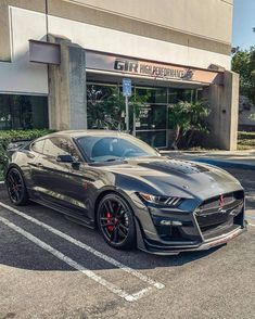 a gray mustang parked in front of a building with black rims and red brake pads