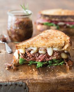 a cut in half sandwich sitting on top of a wooden cutting board next to a jar