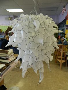 a large white sculpture hanging from the ceiling in a room filled with books and desks