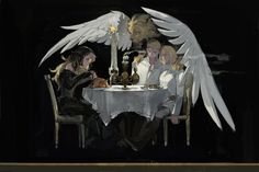 two people sitting at a table with angel wings on their head and one person holding a lit candle