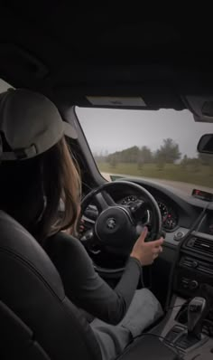 a woman driving a car down a road with her hands on the steering wheel and looking out the window