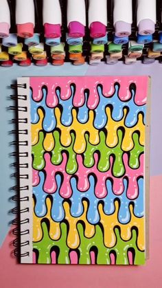 a notebook with colorful designs on it next to some markers and paint bottles in the background