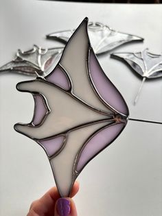 a hand holding a stained glass piece in the shape of a bat on a table