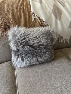 a gray furry pillow sitting on top of a couch next to a throw blanket and pillows