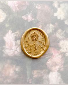 a gold button with an ornate design on the front and back, sitting on a floral background