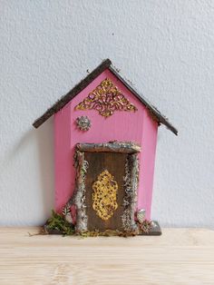 a small pink house sitting on top of a wooden table next to a white wall