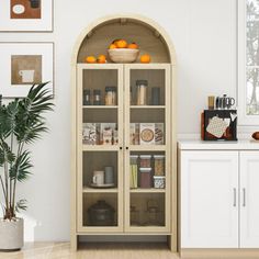 a white kitchen with an arched glass door and wooden shelves filled with spices, condiments and fruit