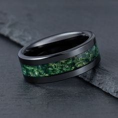 a wedding band with green moss inlay and black ceramic inside, sitting on top of a rock