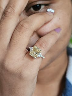 a woman wearing a yellow diamond ring on her finger and holding her hand to her face