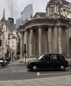 a black taxi cab driving down a street next to tall buildings with columns on them