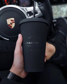 a person holding a cup with a straw in their hand and steering wheel behind them