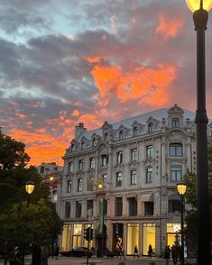 a street light sitting in front of a tall building under a colorful sky with clouds