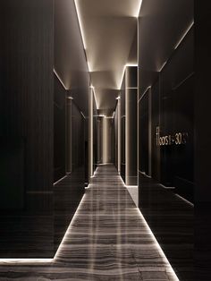 an empty hallway with black walls and wood flooring is lit by recessed lighting