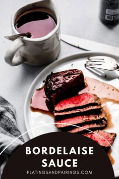 a plate topped with meat and sauce next to a cup of hot chocolate on a table