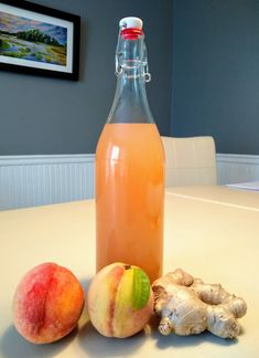 there is a bottle of juice and two peaches sitting on the table next to each other