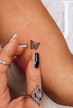 a woman's legs with tattoos and rings on her left arm, next to a butterfly tattoo