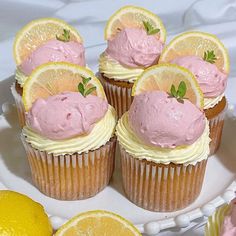 cupcakes with pink frosting and lemon slices on a white plate next to sliced lemons