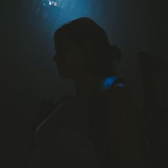 a woman standing in the dark with her back turned to the camera and light shining on her