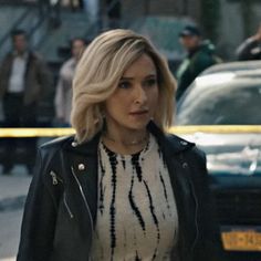 a blonde woman walking down the street in front of police tape and cars behind her