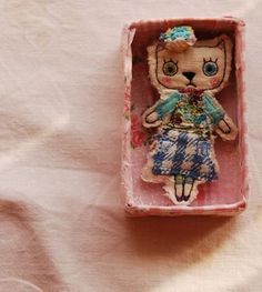 a small doll in a pink box on a white surface