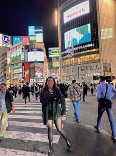 a group of people walking across a cross walk in the middle of a city at night