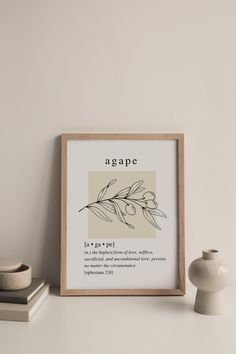 a framed print with the word agape on it next to some books and a vase