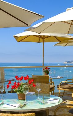 an outdoor dining area overlooking the ocean with umbrellas and flowers in vases on table