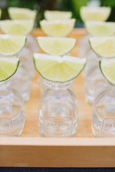 limes are arranged in small glass pitchers on a wooden tray with lemon wedges