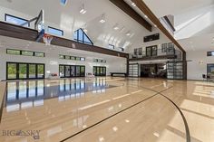 a large indoor basketball court with high ceilings and glass doors on each side, surrounded by wood flooring