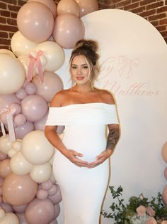 a pregnant woman standing in front of balloons and flowers with her hands on her stomach