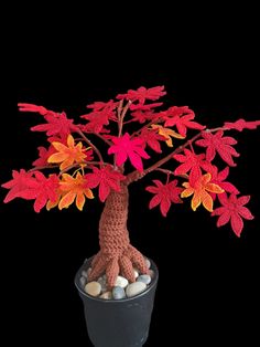 a crocheted tree in a pot filled with rocks and leaves on a black background