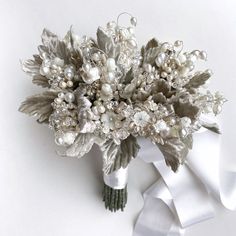 the bridal bouquet is adorned with pearls and silver leafy foliage, along with white satin ribbon