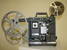 an old fashioned movie projector sitting on top of a white table next to a reel