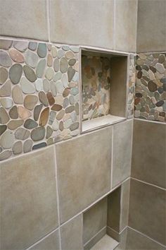 a walk in shower sitting next to a tiled wall covered in stones and pebbles on the floor