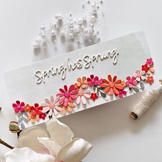 a greeting card with flowers and thread on the edge, next to some white beads