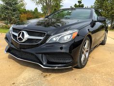 the front end of a black mercedes c - class cab parked in a driveway next to trees