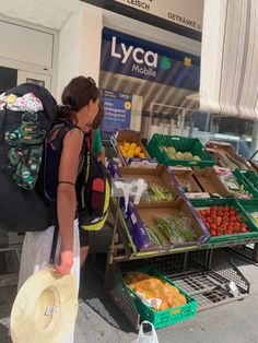 a woman with a hat and backpack looking at produce on display in front of a store